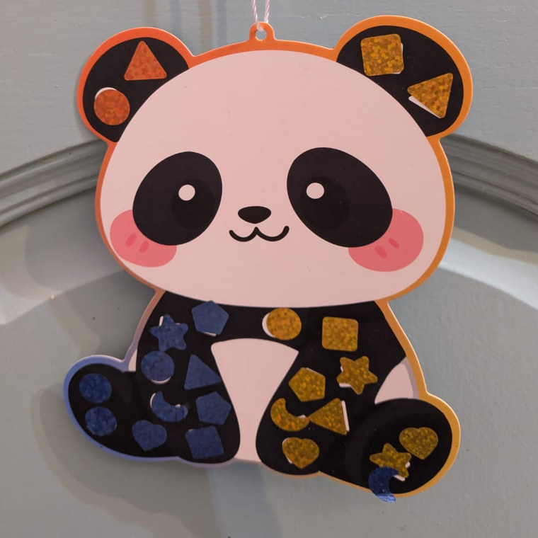 Panda en carton décoré de gommettes pailletées bleues et dorées, suspendu par sa ficelle.